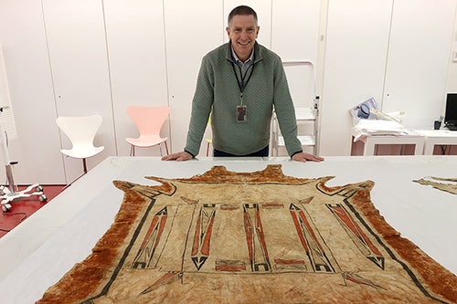 History professor Robert Morrissey in November 2024 at the Musée du quai Branly-Jacques Chirac in Paris with a robe that is an example of the tribes’ hide-painting tradition. Photo courtesy Robert Morrissey