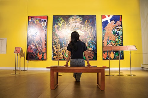 person sitting on bench in front of large paintings
