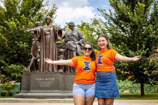 Two Illinois students standing in front of the Alma Mater statue. 