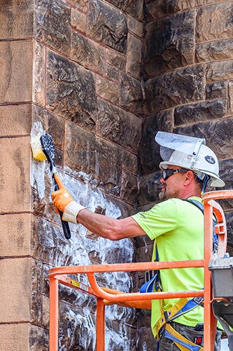 Worker cleans the side of Altgeld Hall with a brush