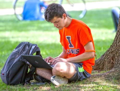 Student working on a computer while sitting under a tree on the Quad