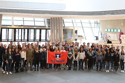 Roughly 75 students who participated in the Illinois in Vienna Program smile while holding a U of I flag.