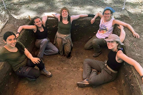 A group of students in a small archaeology pit