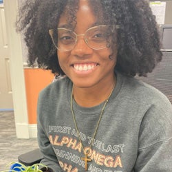 Kristian smiling for the camera. She is wearing a grey sweatshirt and gold-framed glasses.