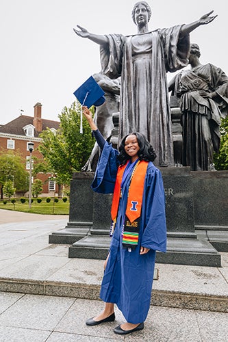 A student on graduation day poses by the Alma Mater