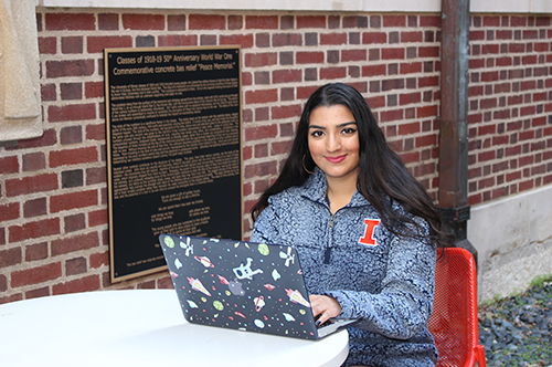 Nidhi Shastri poses while on her computer in front of a brick wall