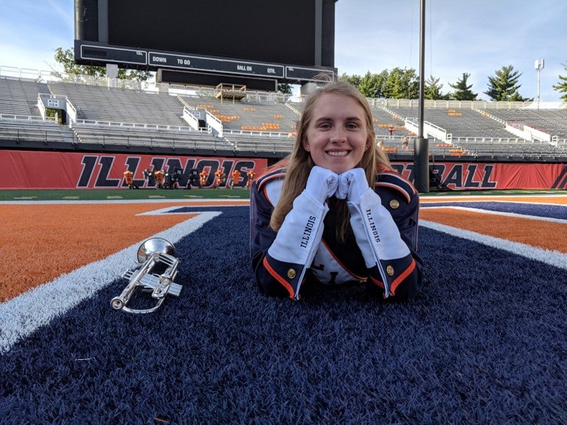 Student poses for photo in Marching Illini uniform on the turf of Memorial Stadium