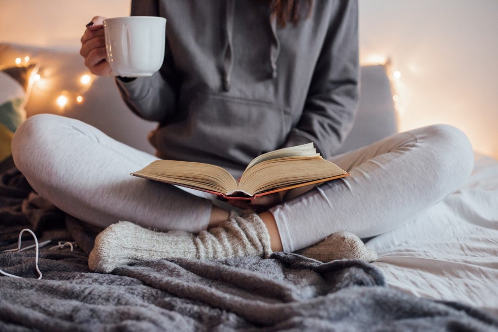 Student reading a book with a cup of tea under a blanket