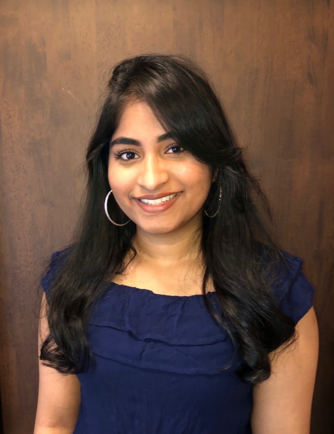 LAS student Sharon Abraham poses for a photo in a blue dress against a wood background.