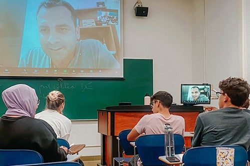 Students listening to a speaker on a projector screen