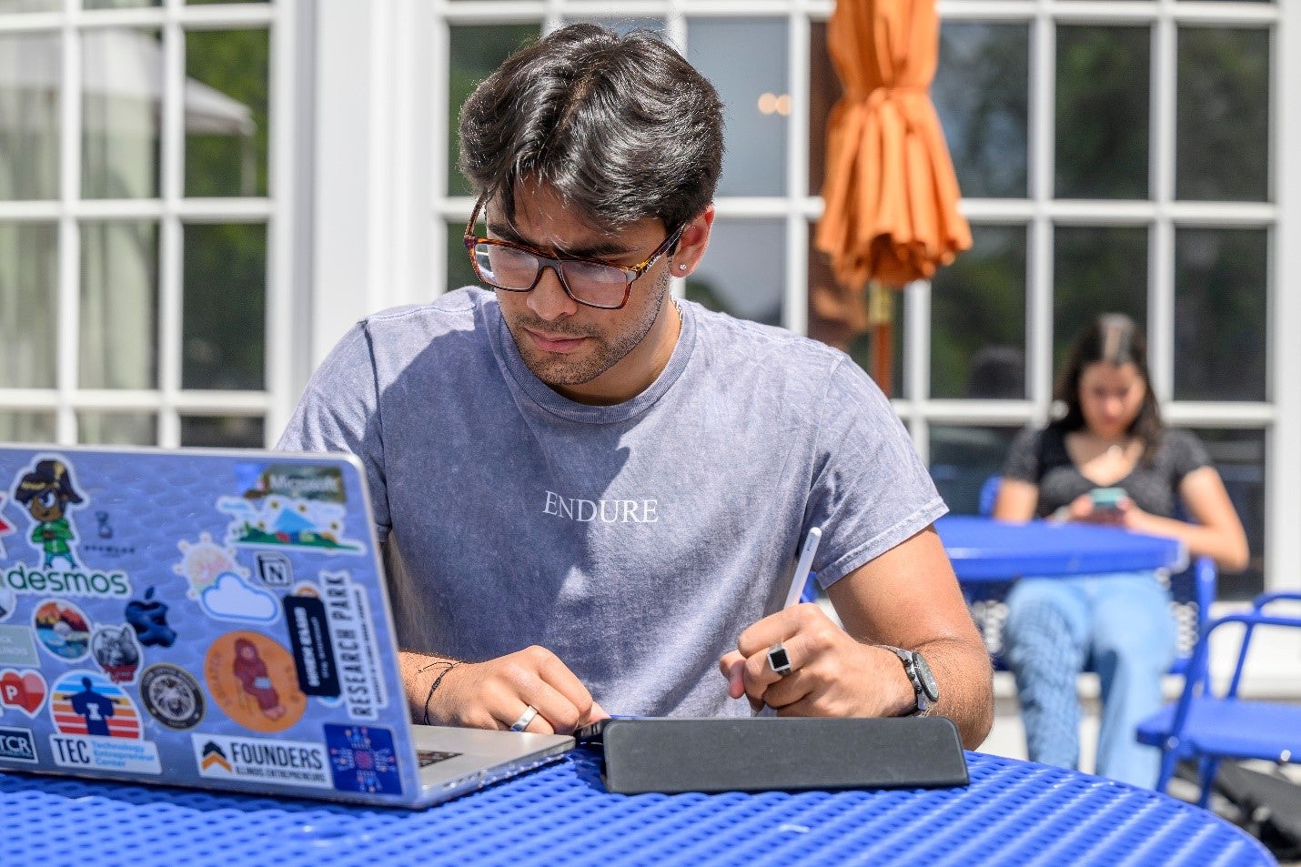 Student with laptop and iPad open, sitting in front of the Quad-facing side of the Union