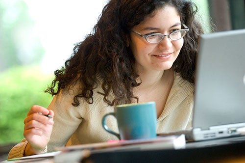 A student works on a computer. A coffee cup is in the foreground.
