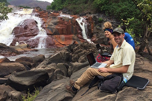 Students with laptops pose near a waterfall in Sierra Leone