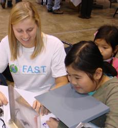 Science students from U of I introduced Chicago-area schoolchildren to the science behind sports at Mayor Daley's annual sports festival this past December. Here, geology student Kristin Read is having children draw while looking in a mirror.