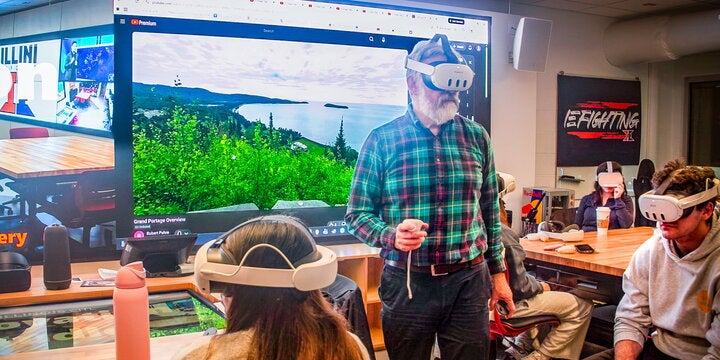 Political science professor Robert Pahre, in virtual reality goggles, talks with students about the VR videos of Yellowstone National Park that he uses to help teach about issues affecting wilderness sites