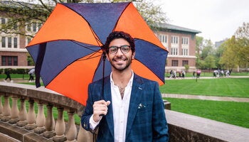 Student in front of Foellinger auditorium holding an orange and blue umbrella