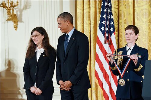 Former President Barack Obama looks at May Berenbaum as a woman in a military uniform holds the National Medal of Science 