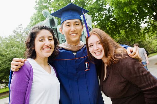 Graduates stand in front of the Alma Mater statue.