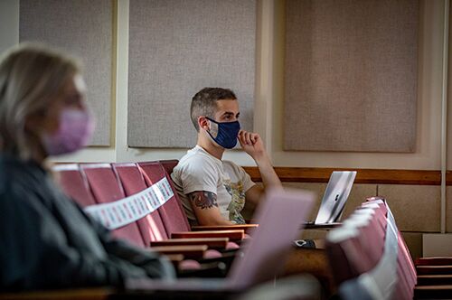 Students sit in a lecture hall while socially distanced and wearing masks
