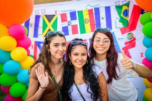 Three students standing in front of different flags of Latin American and Caribbean countries