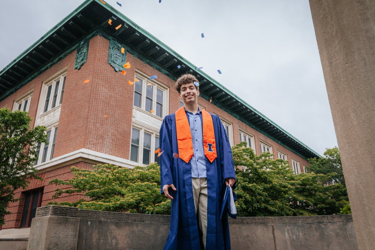 Student in graduation regalia standing at the side of the exterior of Lincoln Hall.