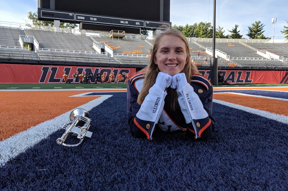 Student poses for photo in Marching Illini uniform on the field at Memorial Stadium