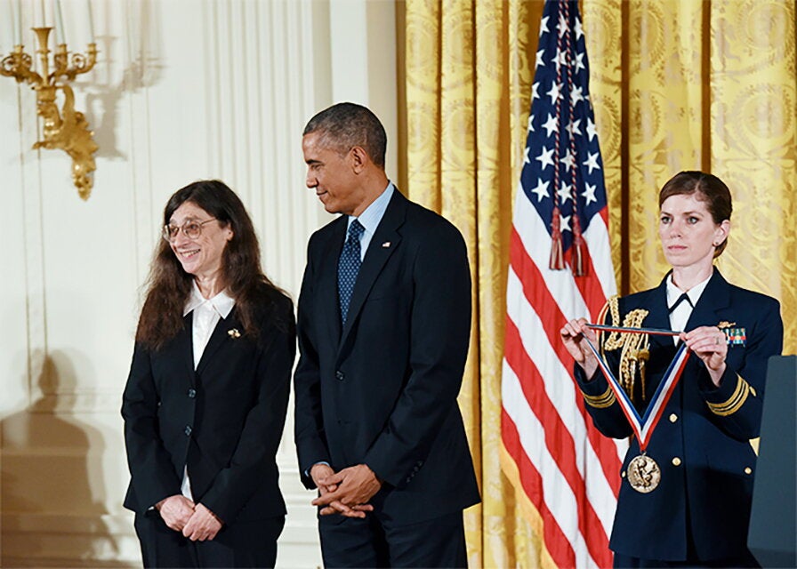 Former President Barack Obama looks at May Berenbaum as a woman in a military uniform holds the National Medal of Science