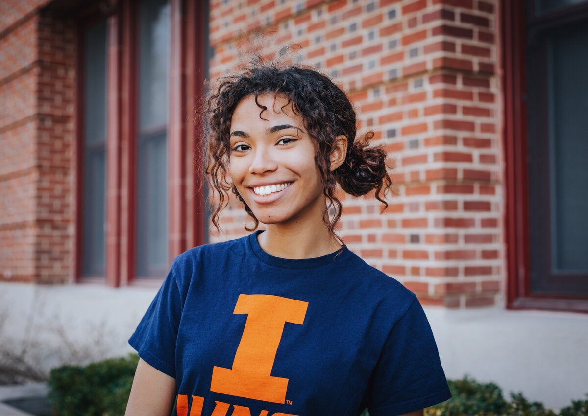 Student smiling, standing in front of Lincoln Hall in blue Illini t-shirt.
