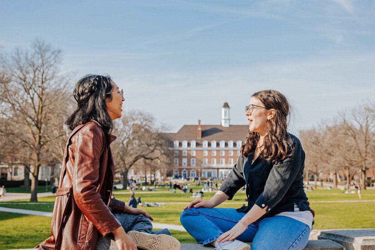 Two students sitting in front of Foellinger Auditorium facing the Illini Union on the Main Quad.