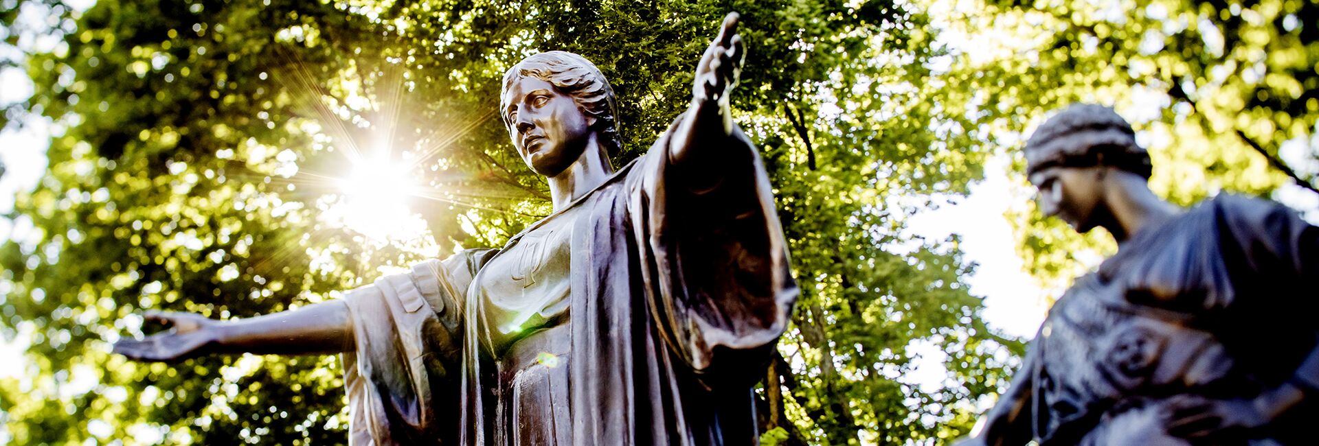 The sun gleams behind the statue of the Alma Mater