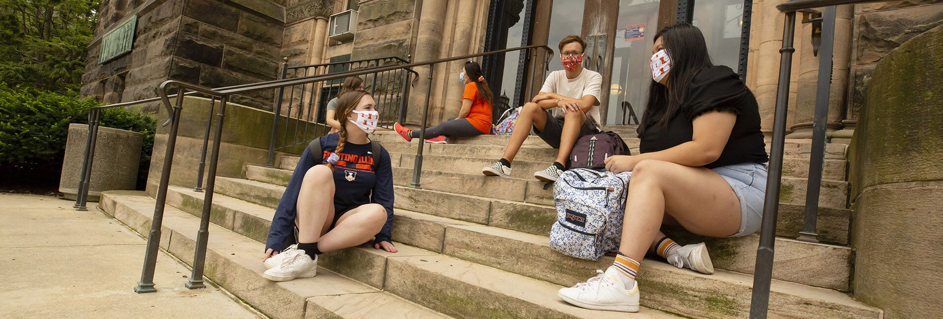 Students chat on the steps to Altgeld Hall. They are wearing masks.
