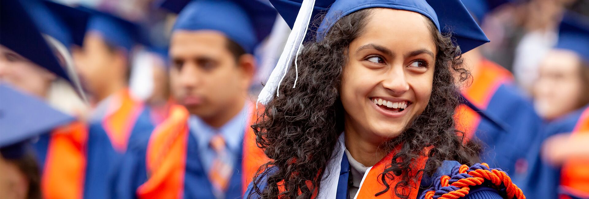 A student wearing a cap and gown smiles