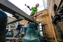 Workers removing the Altgeld bells. A man in a hard hat stands above a bell, getting ready to remove it