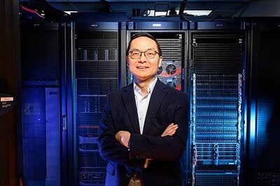 Huimin Zhao, a professor of chemical and biomolecular engineering at the University of Illinois Urbana-Champaign, stands in front of computer towers.
