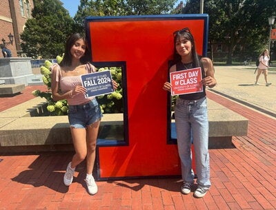 Ariana and her older sister in front of a Block-I with signs reading "Fall 2024" and "First Day of Class". 