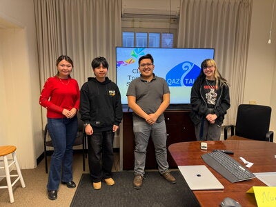 Four people standing in front of a screen at Coble Hall for QazTalk.