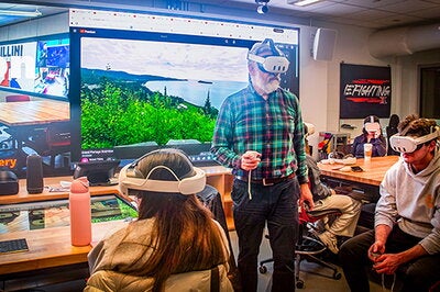 Robert Pahre wearing virtual reality goggles in front of a screen showing wilderness