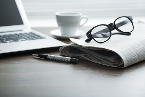 Glasses, newspaper, and a laptop