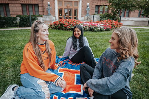 Three girls sitting on the grass on the Quad in front of Lincoln Hall