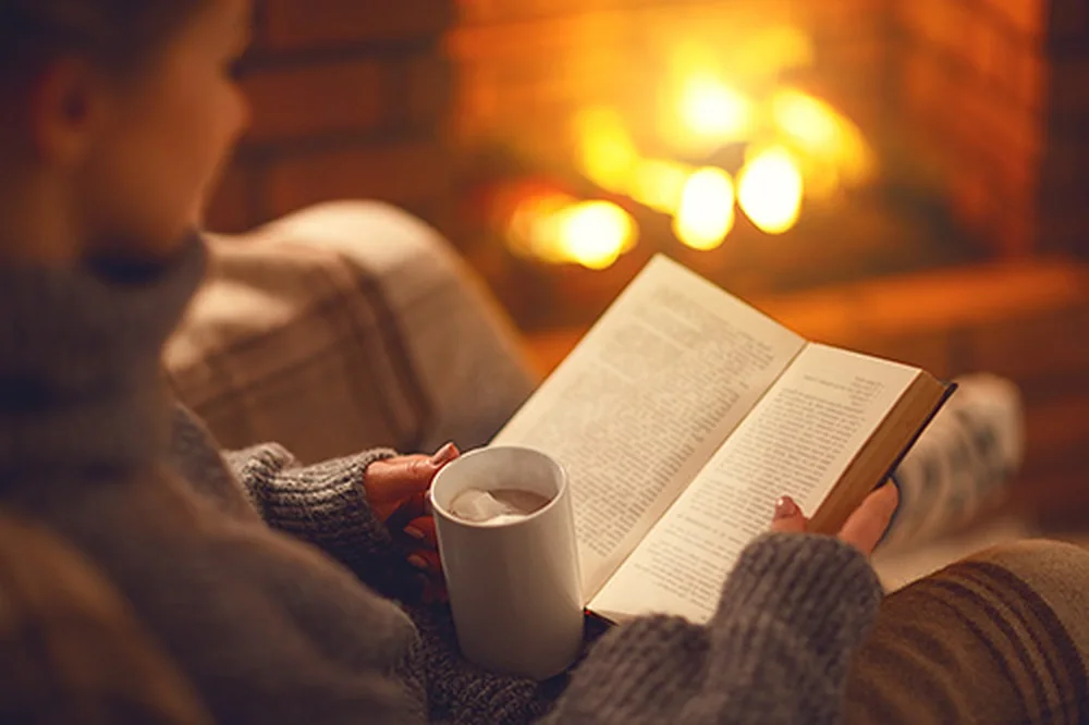 A woman reads a book by the fire