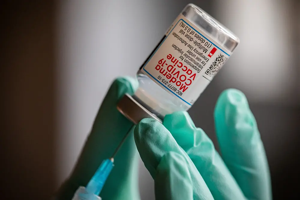 gloved hands holding vial of vaccine