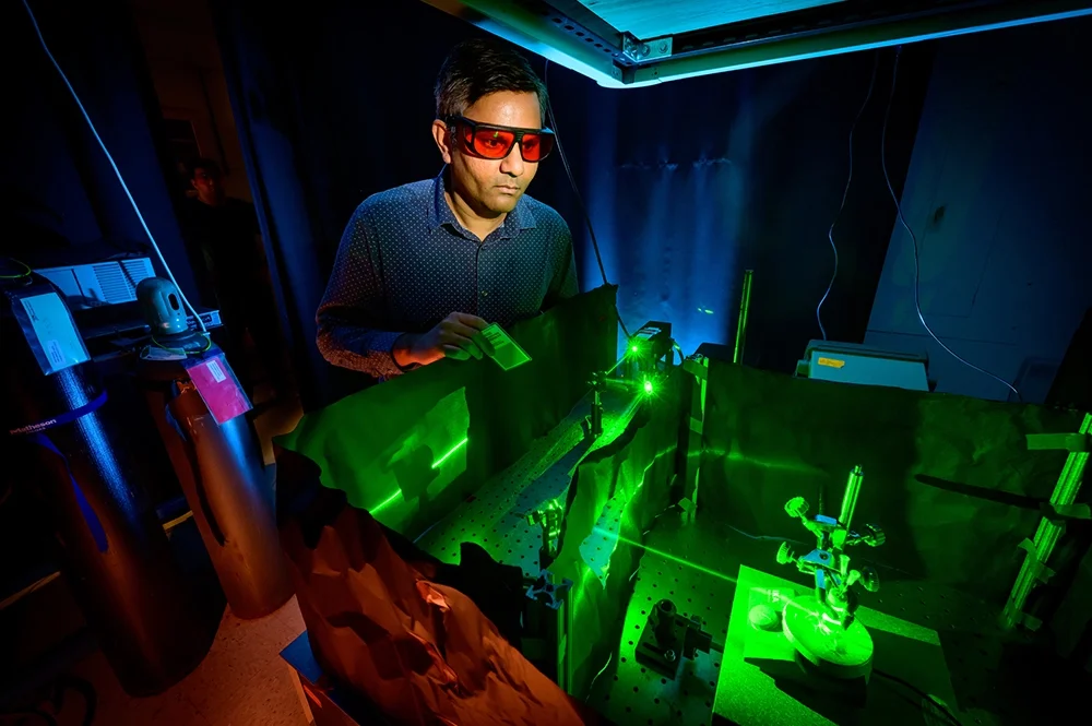 Researcher wearing protective glasses while using a laser to activate an specialized electrochemical reaction inside of an reaction cell.
