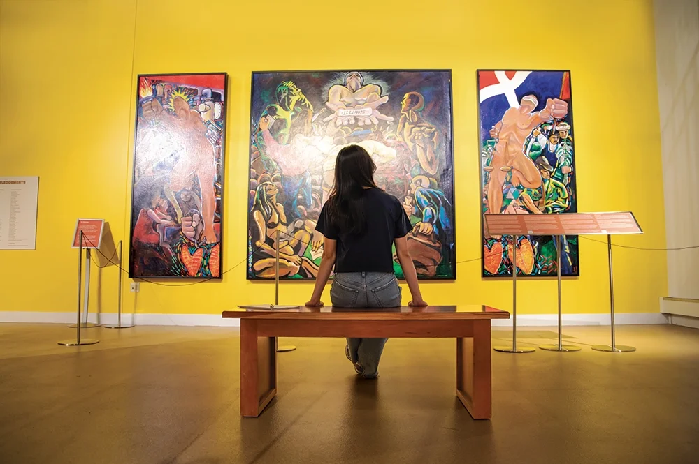 person sitting on bench in front of large paintings
