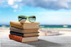 A stack of books on a picnic table next to the beach