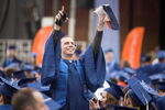 Student in blue cap and gown raising his arms in the air at graduation ceremony