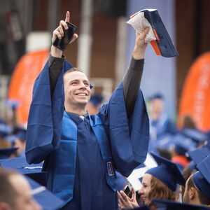 Student in blue cap and gown raising his arms in the air at graduation ceremony