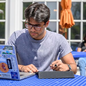 Student with laptop and iPad open, sitting in front of the Quad-facing side of the Union